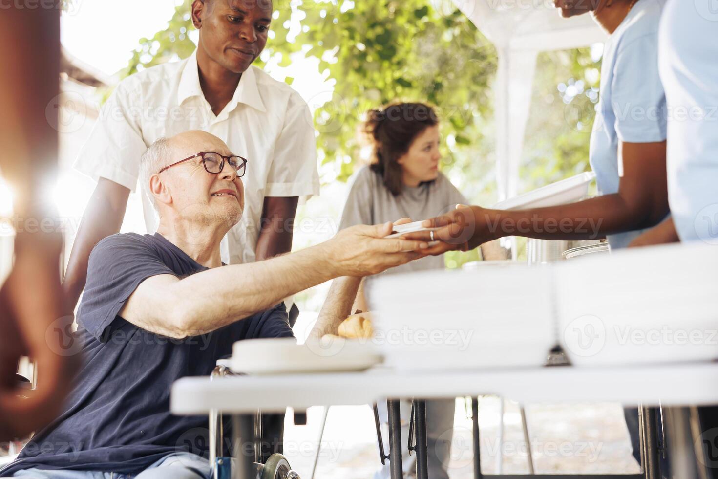 Charitable organisation gives assistance and free meals to homeless individuals, demonstrating dedication to fighting hunger and poverty. Volunteers provide a warm food to caucasian wheelchair user. photo