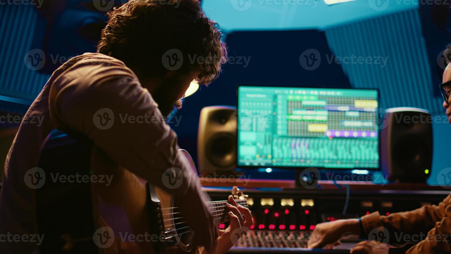 Young artist songwriter composing a new song on guitar in recording session at studio, creating tunes and editing them after in post production. Musician composer producing tracks. Camera B. photo