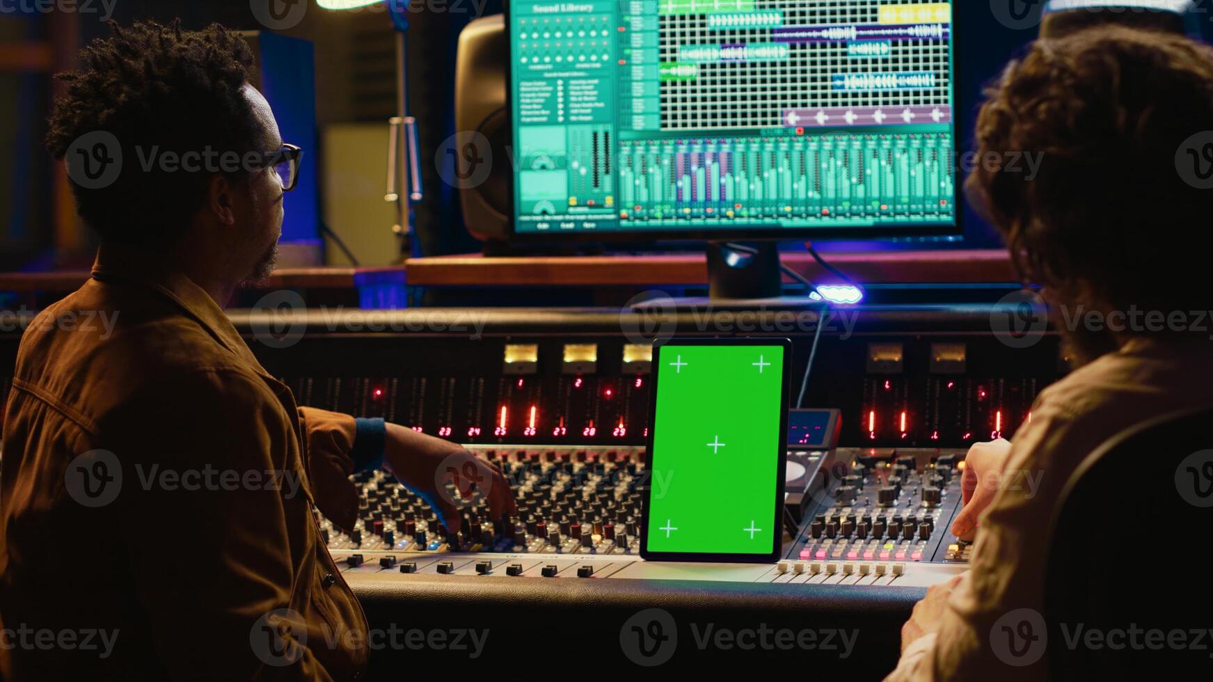Team of producer and artist use tablet with mockup display in professional studio, mixing and mastering tracks after recording session. Experts working in control room with console. Camera A. photo