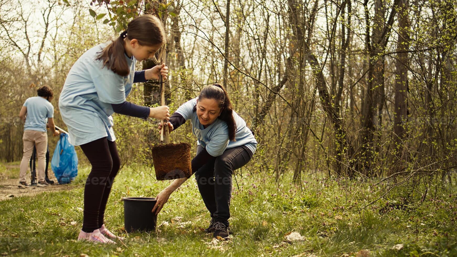 Mother and daughter team up to plant new trees in the woods, protecting the natural habitat and ecosystem. Family of activists fighting nature conservation, digging holes for seedlings. Camera B. photo