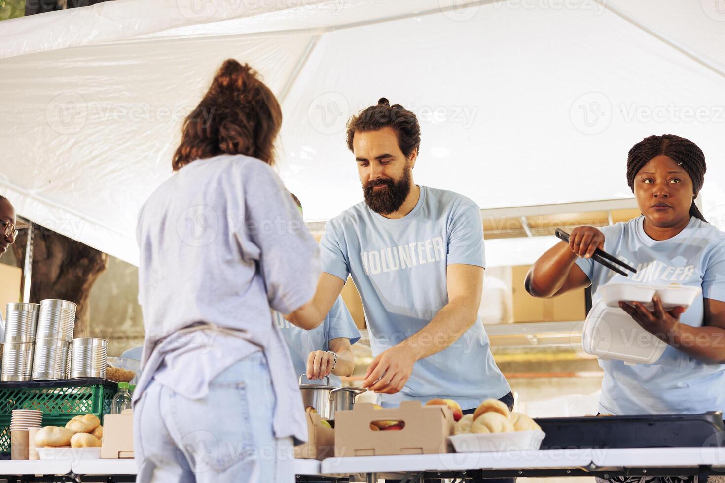 Charitable volunteers distributing free meals to homeless and needy individuals at an outdoor local food bank. Hunger relief team supporting and providing food assistance to the less fortunate. photo