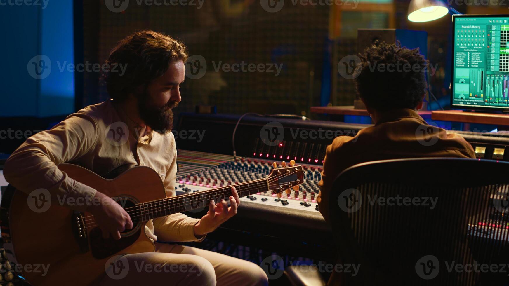 Creative artist singing on his electro acoustic guitar to record new track, producing music in control room at professional studio. Skilled musician composer creating new songs for an album. Camera A. photo