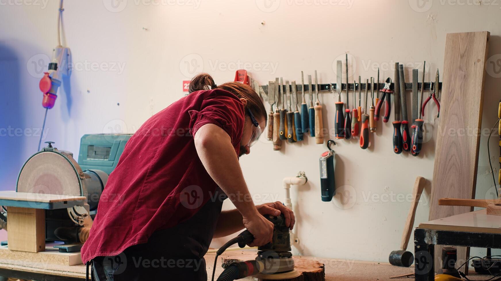 Carpenter wearing safety glasses giving clipboard with blueprints to assistant, using angle grinder on wood. Man with protective goggles using orbital sander gear after consulting schematics, camera A photo