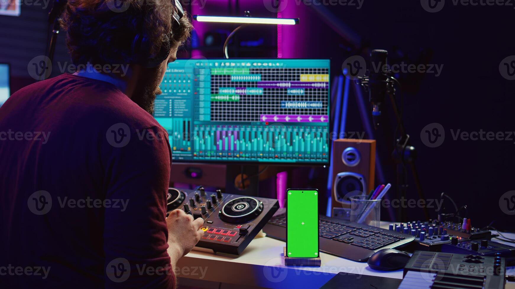 Sound engineer working on mixing and mastering techniques in his home studio, using phone with greenscreen display while he is recording audio. Artist operating soundboard and amplifier. Camera B. photo