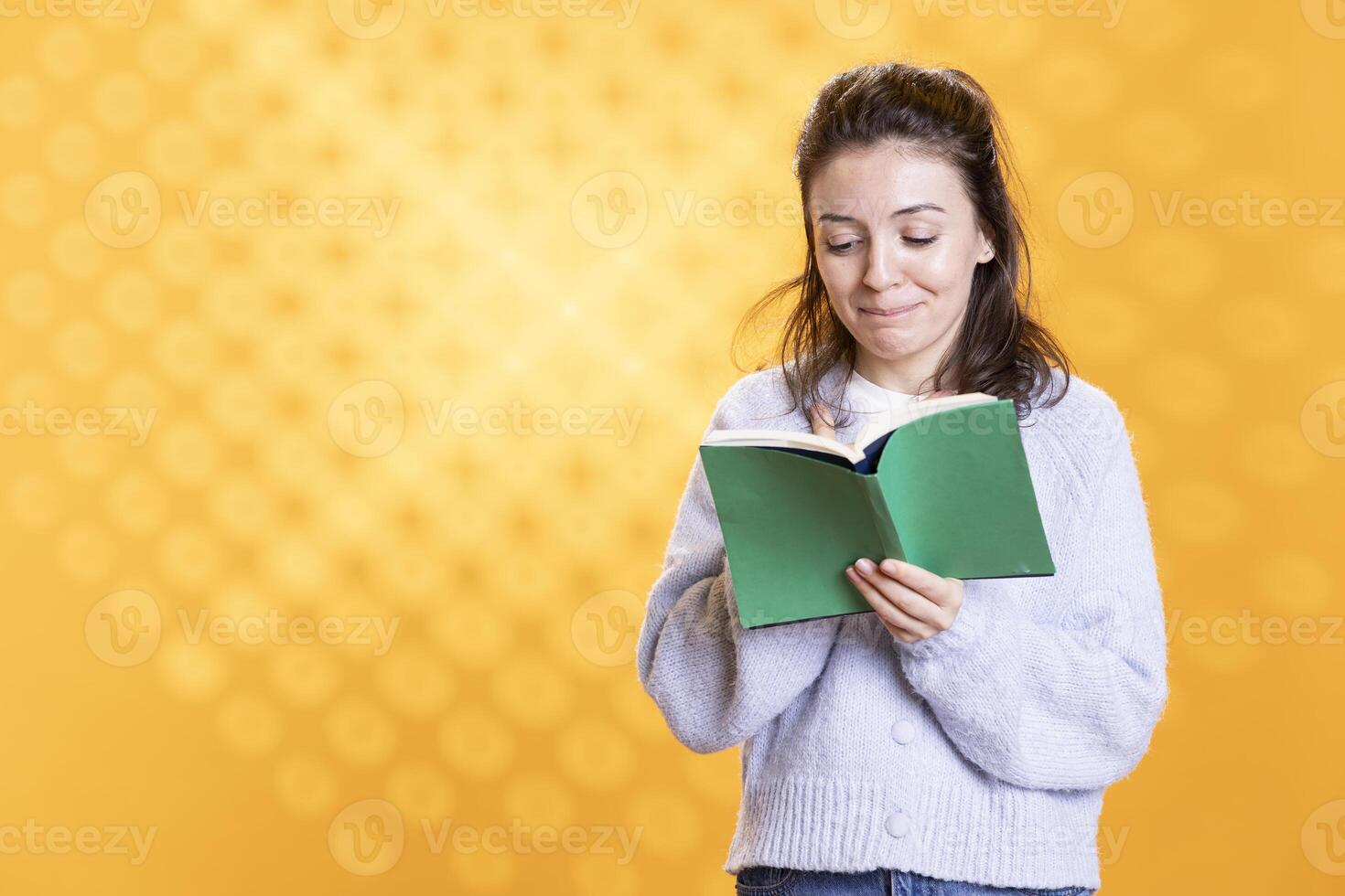 Woman laughing while reading funny book, enjoying hobby during leisure time. Bookaholic person with novel in hands chuckling, amused by comedic story, isolated over studio background photo