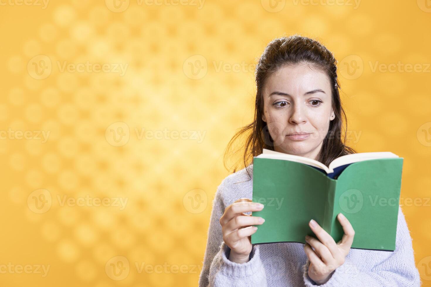 Woman turns page on book, opening eyes wide in amazement, enjoying story, conveying joy of reading concept, studio background. Geek astonished by surprising novel, showing appreciation for literature photo