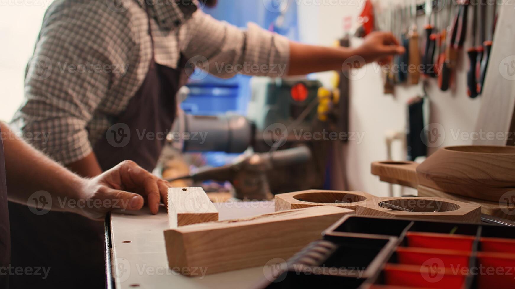 Woodworker using power drill to create holes for dowels in wooden board, close up. Carpenter sinks screws into wooden surfaces with electric tool, doing precise drilling for seamless joinery, camera B photo