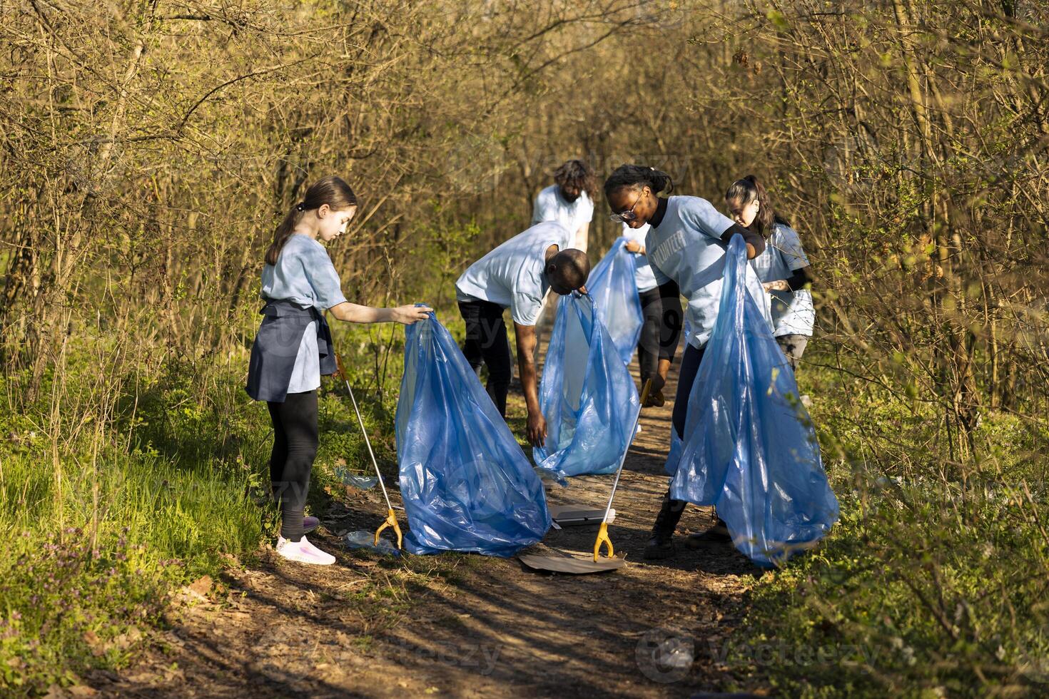 Group of diverse volunteers collecting rubbish and plastic waste, using bags to recycle and gather all junk from the forest habitat. Activists collaborating to clear the woods area from trash. photo