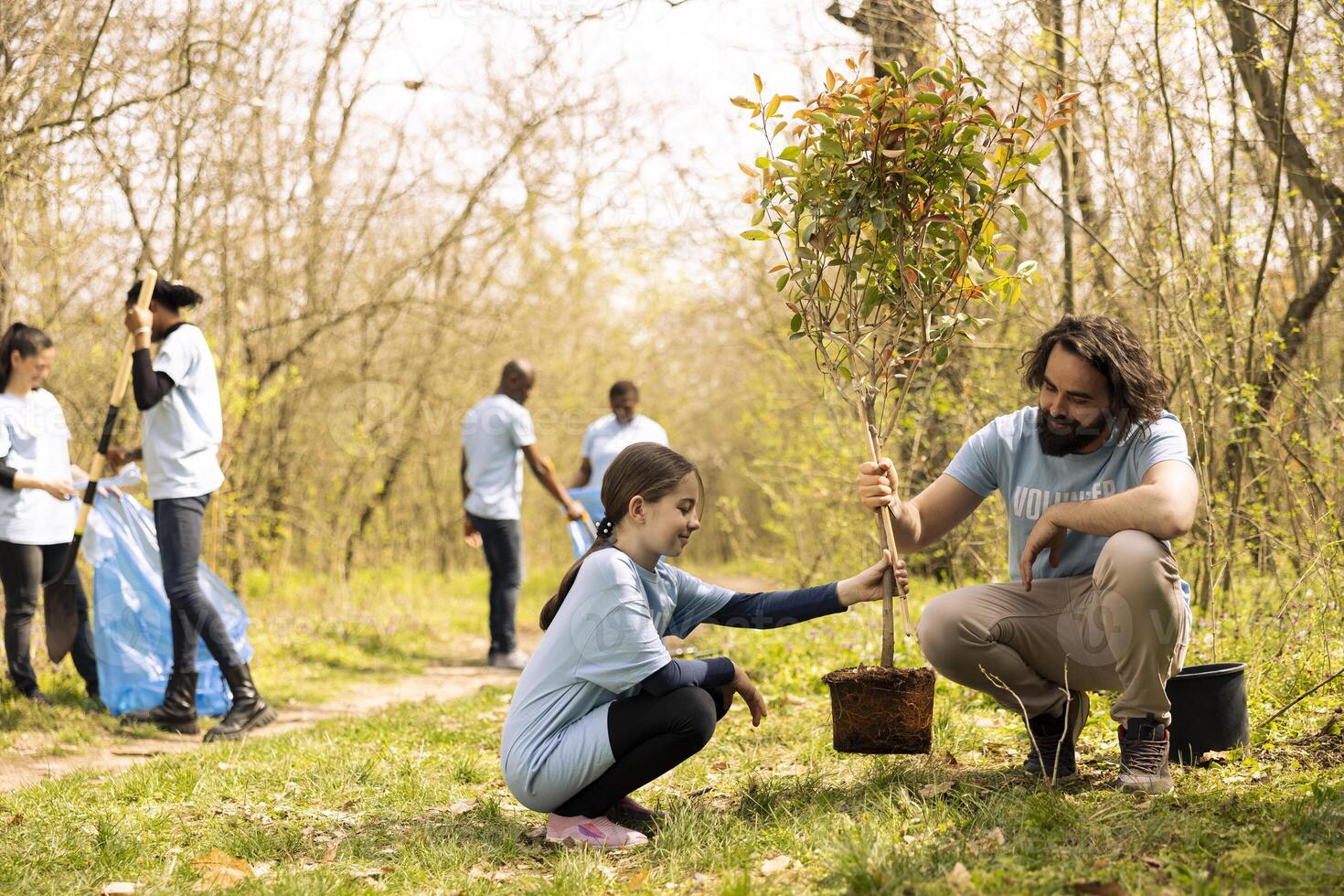 Man and little girl team up and plant a tree together in the woods, preserving the natural environment. People volunteering to help forest ecosystem grow and preserve wildlife. photo