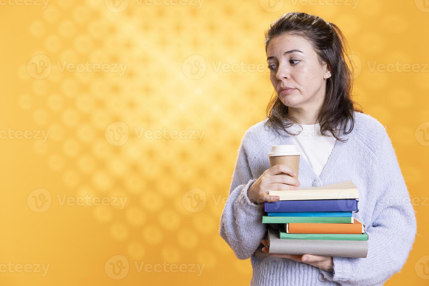 Portrait of woman with stack of books in hands holding disposable cup of coffee, isolated over studio background. Bookworm holding pile of novels and caffeinated drink early in the morning photo