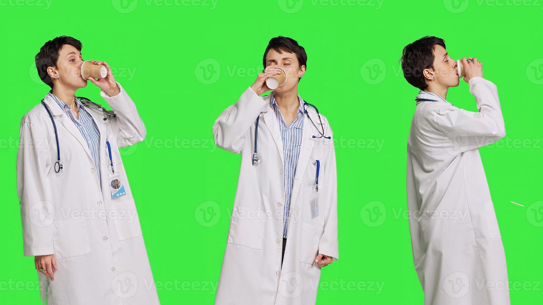 Happy medic serving hot coffee cup as refreshment against greenscreen backdrop, wearing white coat and drinking caffeine beverage. General practitioner enjoying drink, medical expertise. Camera B. photo