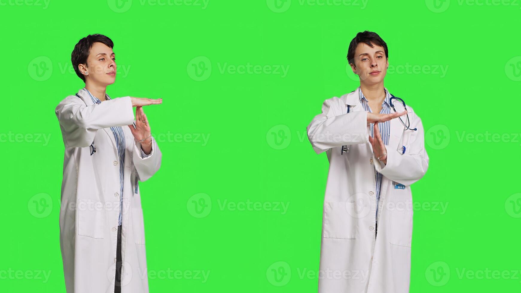 Woman physician doing timeout gesture against greenscreen backdrop, asking for a work break after multiple examinations. Doctor showing pause or stop symbol, feeling tired. Camera B. photo