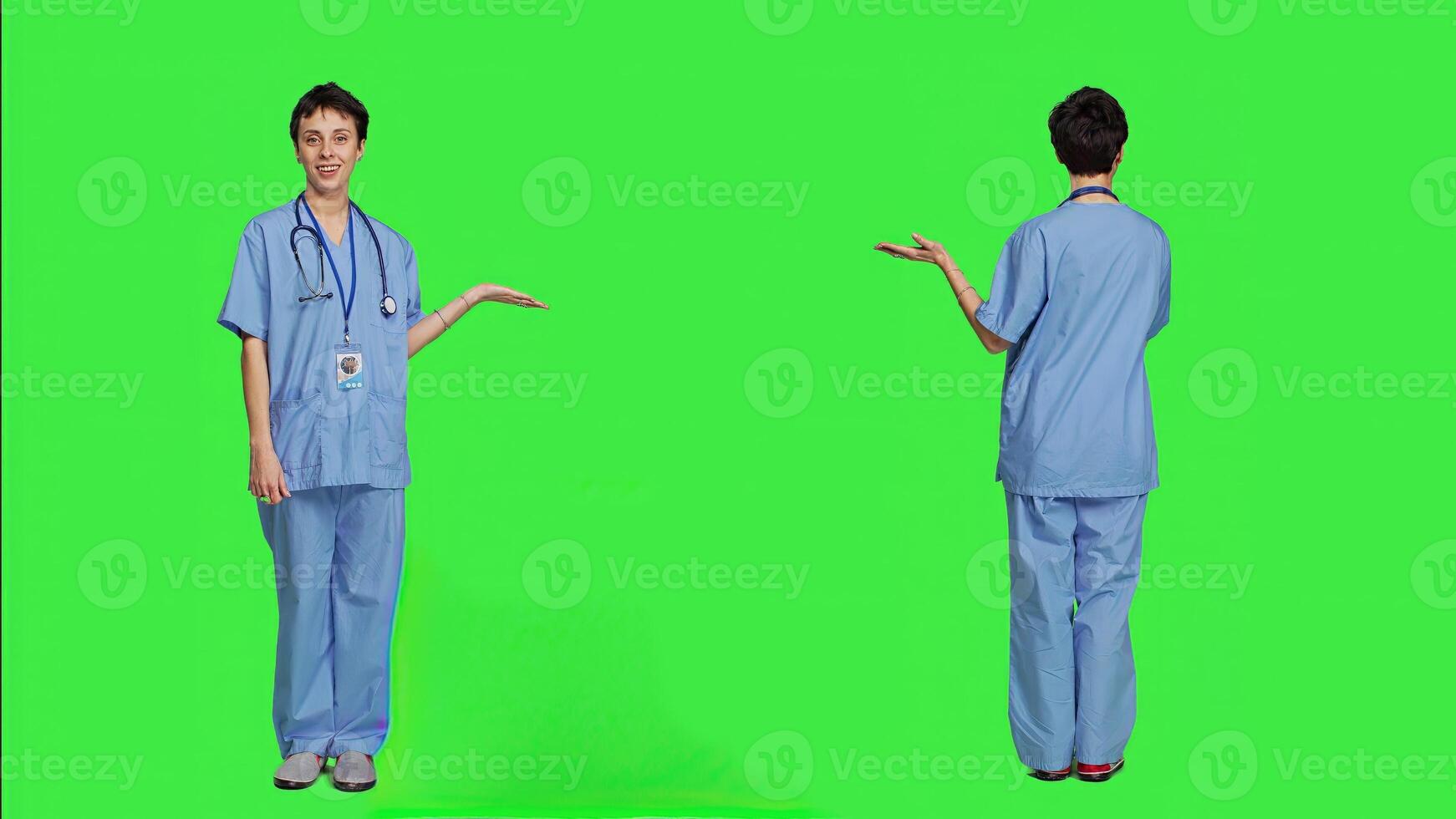 Medical assistant pointing at something aside and doing web commercial, creating advertisement against greenscreen backdrop. Young nurse with scrubs showing a thing to left or right sides. Camera A. photo