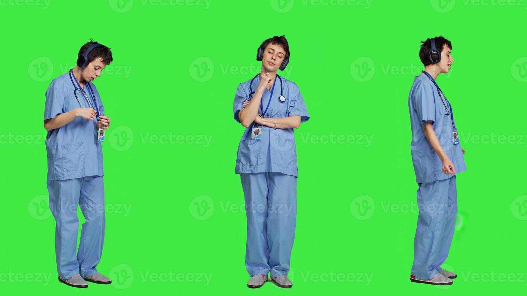 Cheerful health specialist listening to cool music on audio headset, dancing against greenscreen backdrop and having fun. Nurse enjoying songs an doing funny dance moves, leisure. Camera A. photo