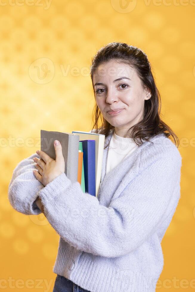 Portrait of happy woman hugging stack of textbooks, gathering information for school exam, isolated over studio background. Jolly person holding pile of books, preparing for university assessment photo