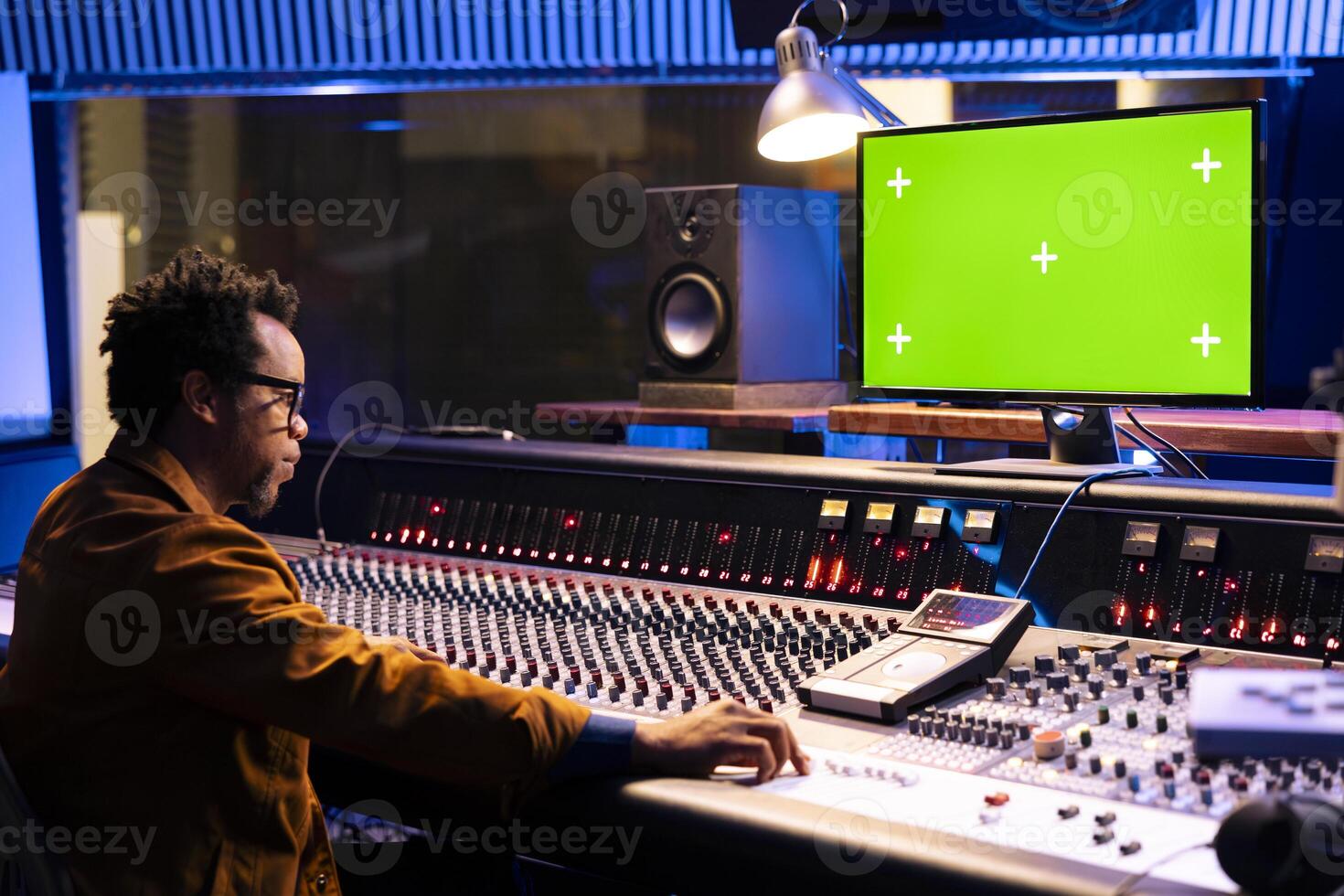 Sound designer operating mixing console and greenscreen monitor, twisting various knobs and buttons in professional studio. Audio technician editing tracks in post production, technical gear. photo