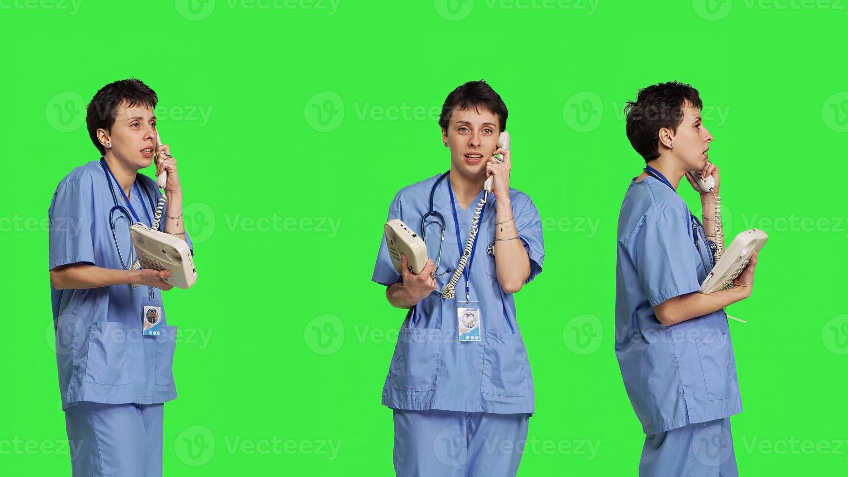 Nurse answering landline phone call to make checkup appointments, talking to patients on telephone with cord against greenscreen backdrop. Health specialist in scrubs uses vintage phone. Camera B. photo