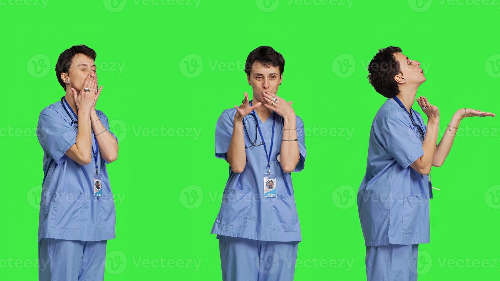 Flirty cute nurse blowing air kisses against greenscreen backdrop, being romantic and expressing sweet feelings. Medical assistant in scrubs doing lovely gesture, expressing true love. Camera B. photo