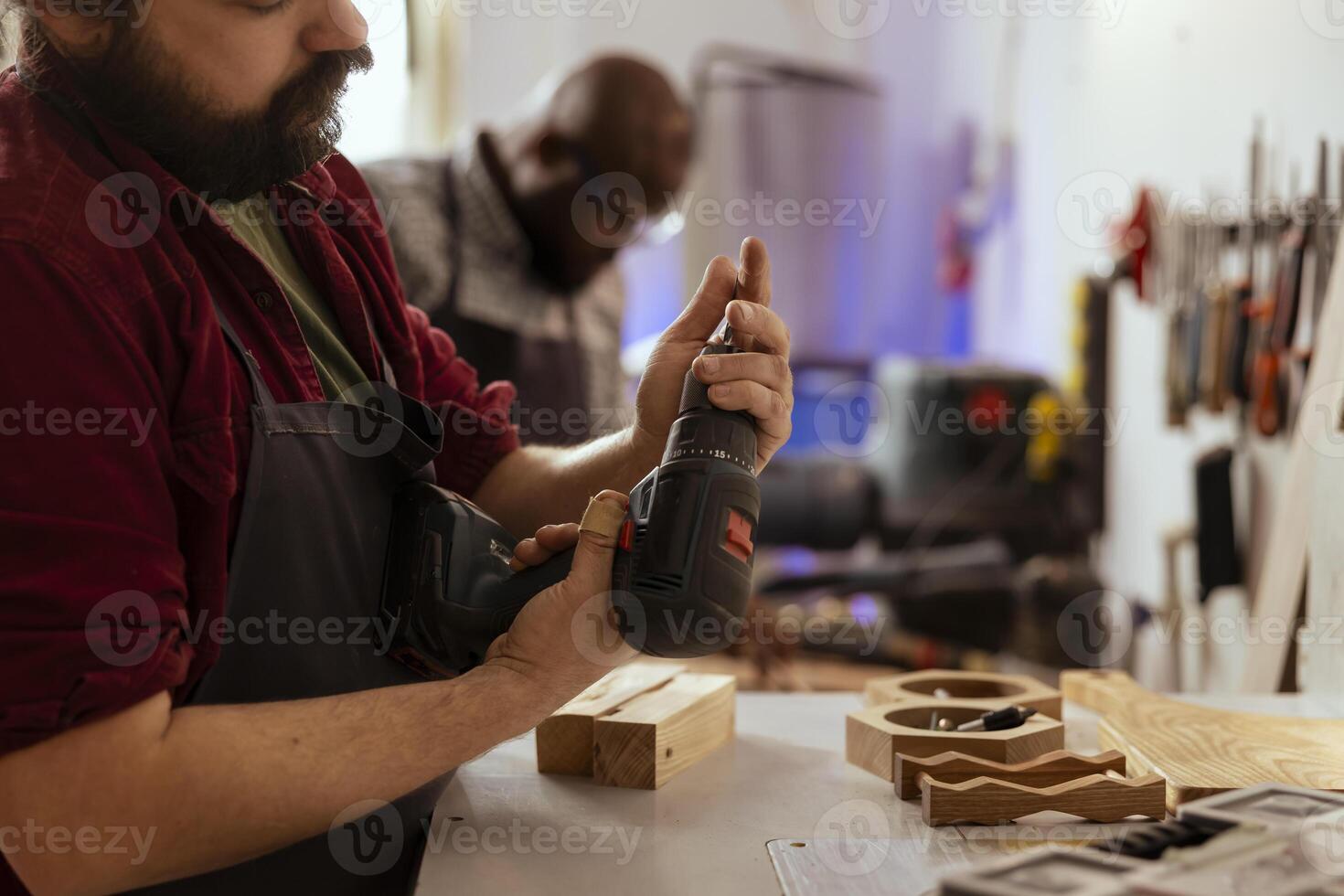 carpintero cambiando poder perforar cabeza dentro adecuado uno para tarea adelante, haciendo agujeros dentro madera bloquear. ebanista en montaje tienda preparando eléctrico engranaje herramienta a utilizar para oficial trabajo foto