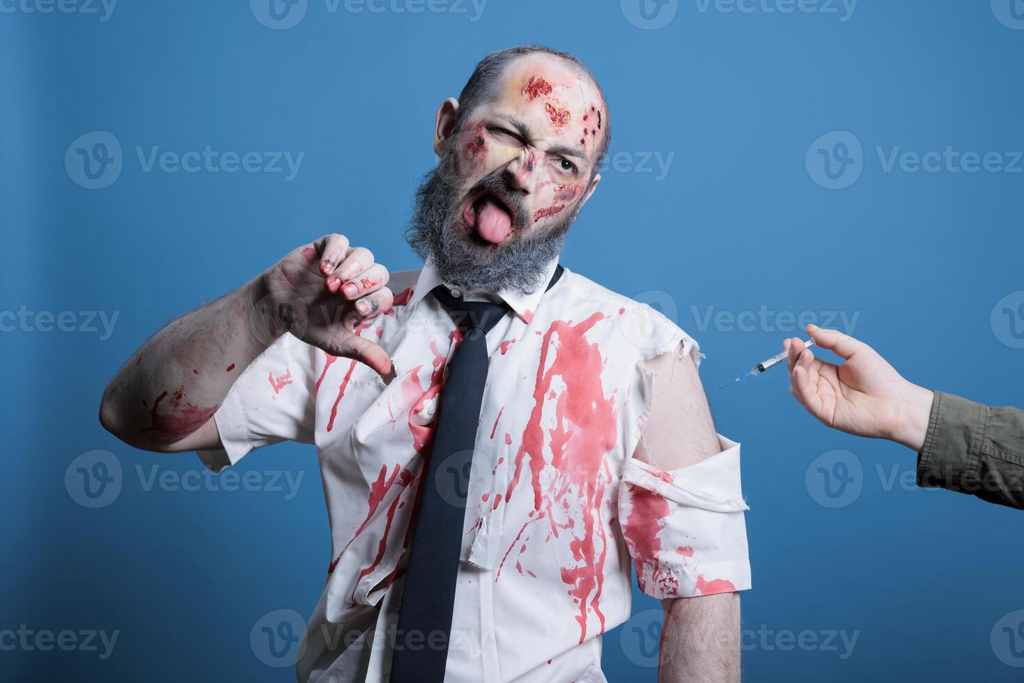 Man forced to take coronavirus vaccine shot showing thumbs down, conspiracy theory concept. Antivaxxer person receiving injection against will, showing disapproving hand gesture, studio background photo