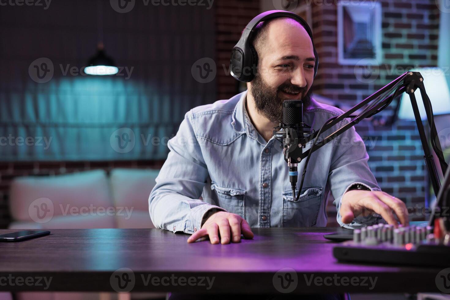 Experienced radio host playing music in professional on air home studio with neon lights, entertaining audiences. Dj using high quality setup to produce and distribute musical pieces photo