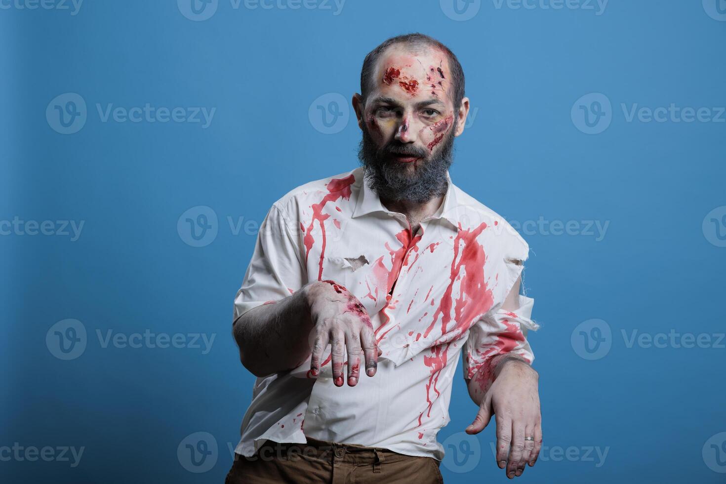 Man dressed as spooky zombie for Halloween event looking ferocious and frightening. Person costumed as undead demon covered in blood and scars looking dangerous, studio background photo