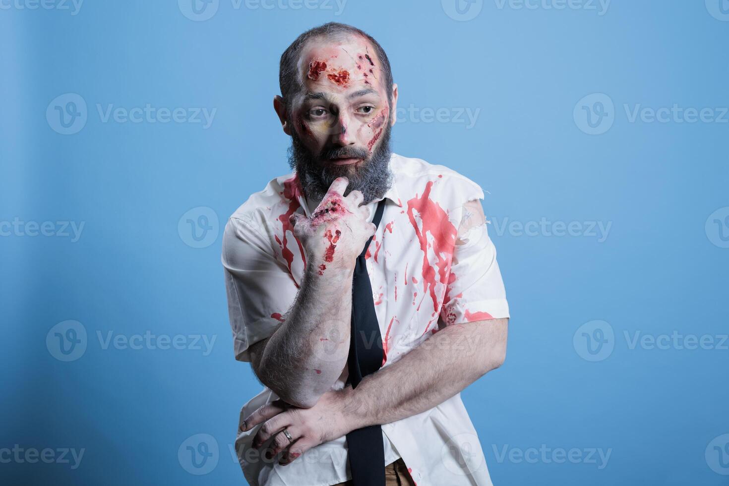 Actor dressed as horror movie brainless zombie repeating lines between scenes on set. Man costumed as mindless infected creature preparing for role, isolated over studio background photo