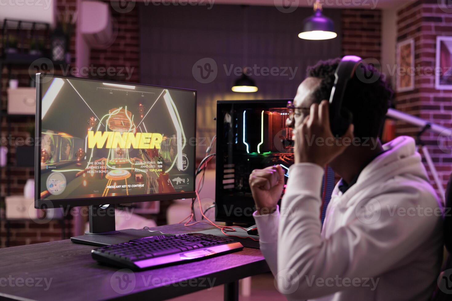 African american gamer excited about winning online multiplayer match against other players. Man seeing winner message on gaming PC computer display in neon lights living room photo