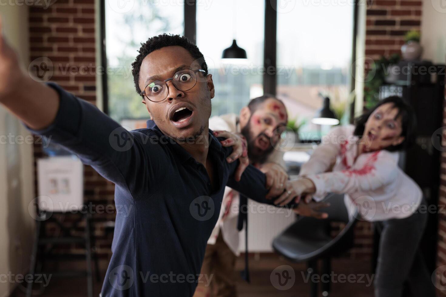 Close up of african american businessman grabbed by scary undead monsters in company office. Focus on apocalypse survivor pulled by brain eating zombies in blurry background photo