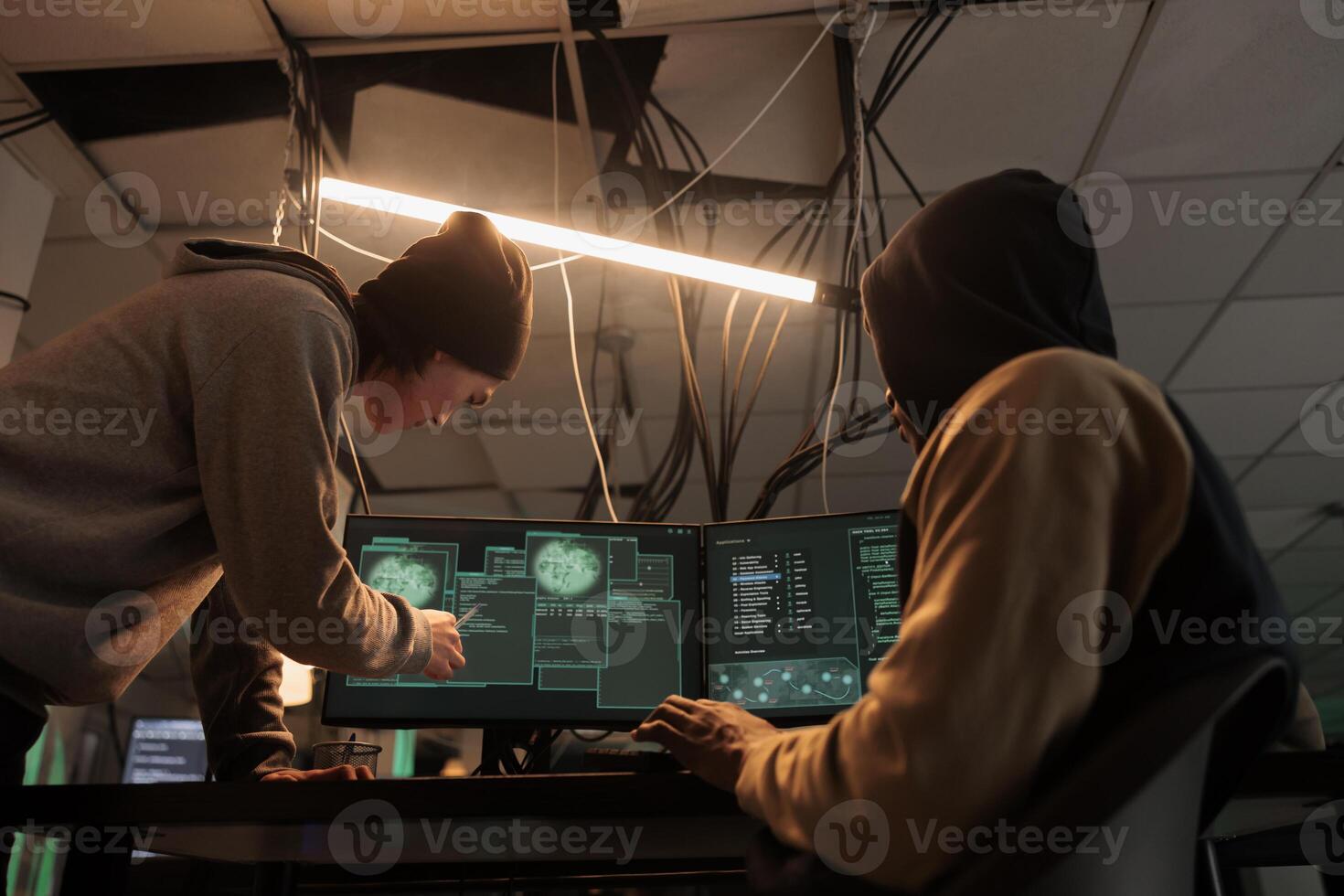 Hackers team hacking online server, stealing data, cybercrime. Cyberattack, it specialist pointing at code on pc screen, criminals programming internet virus at night time photo
