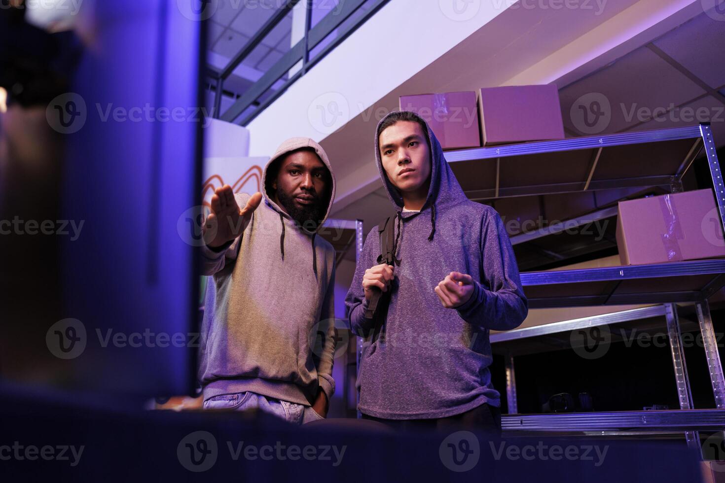 Hackers looking at computer and planning phishing attack. Criminals pointing at screen and discussing ransomware for fraud illegal activity in abandoned warehouse at night photo