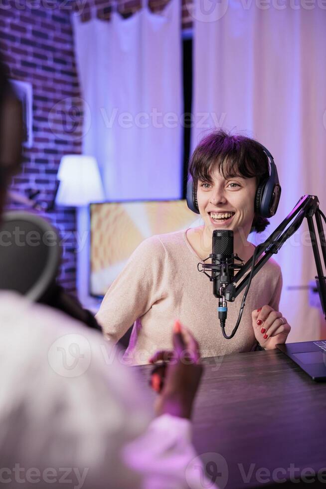 Happy women meeting in studio to record podcast show with professional sound equipment. Vlogger and guest broadcasting live chat to create comedic internet channel content together photo