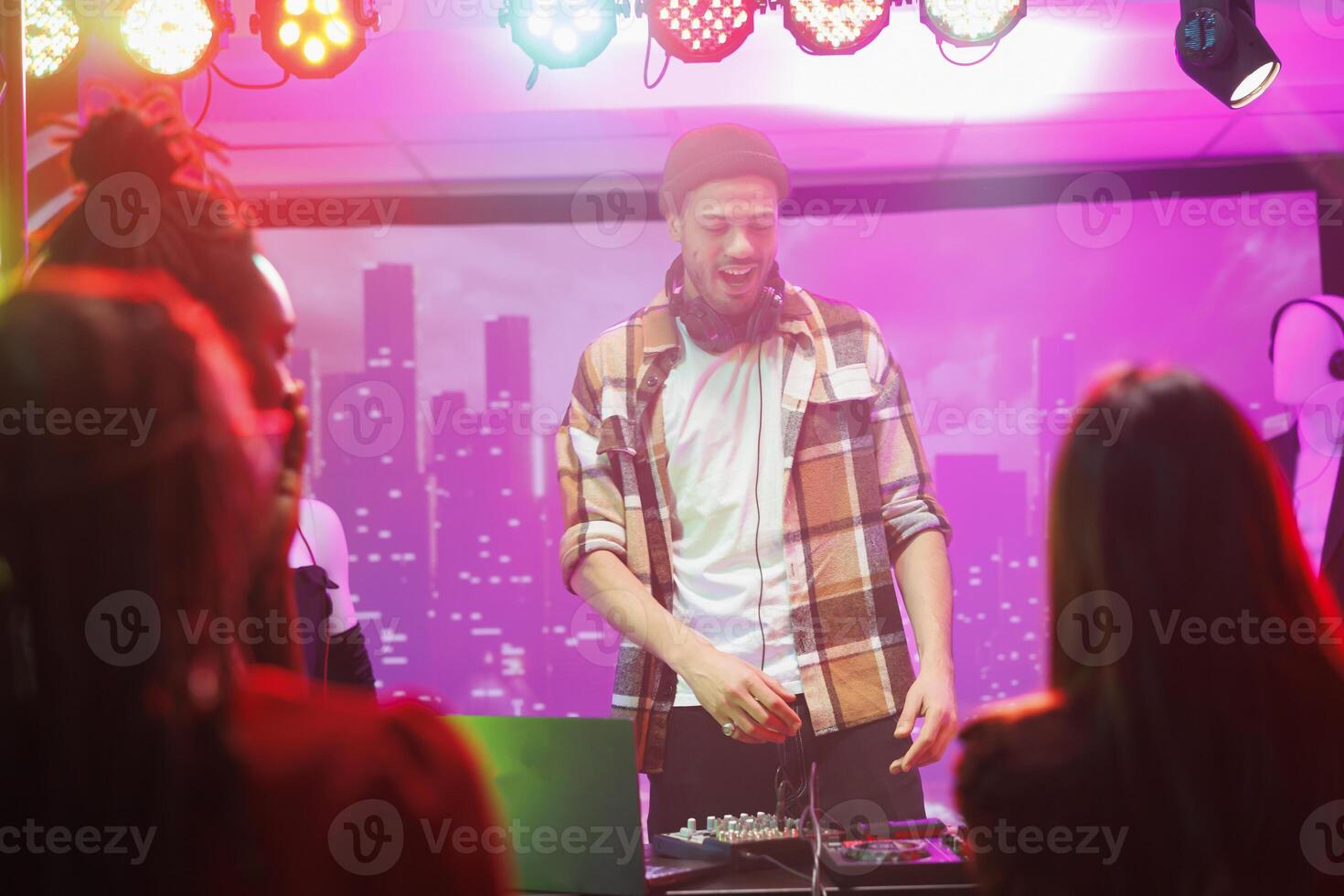 Dj on stage controlling music while crowd partying and dancing in nightclub. Man musician mixing sound on console while performing at live concert in club with spotlights photo