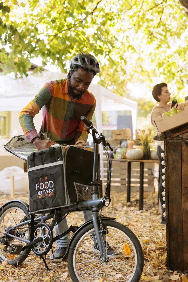 Delivery of fresh fruits and vegetables by african american courier. Young black man picking up an order from the farmers market and delivering healthy local food to customers. photo