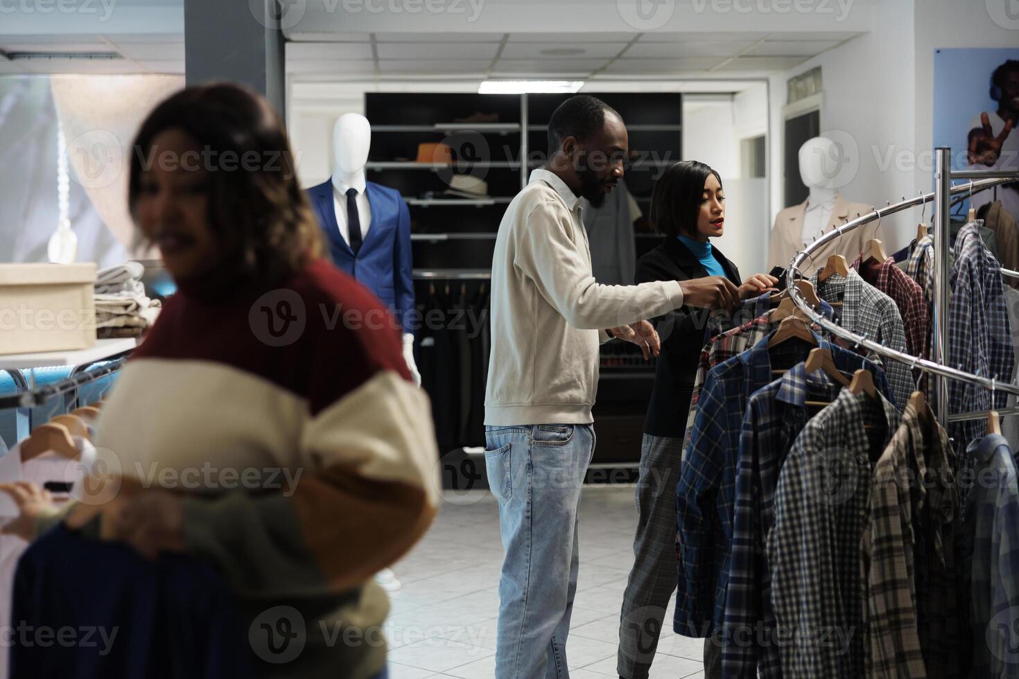 Clothing store assistant and buyer browsing apparel rack together while choosing casual trendy outfit. Boutique asian woman worker offering client advice in selecting shirt size photo