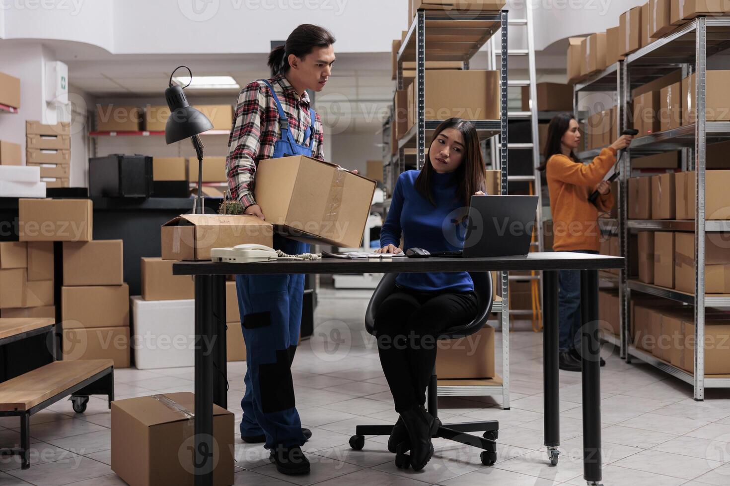 Warehouse asian operators team managing package delivery in storage room. Storehouse worker holding parcel ready for transportation and woman coworker scheduling shipment photo