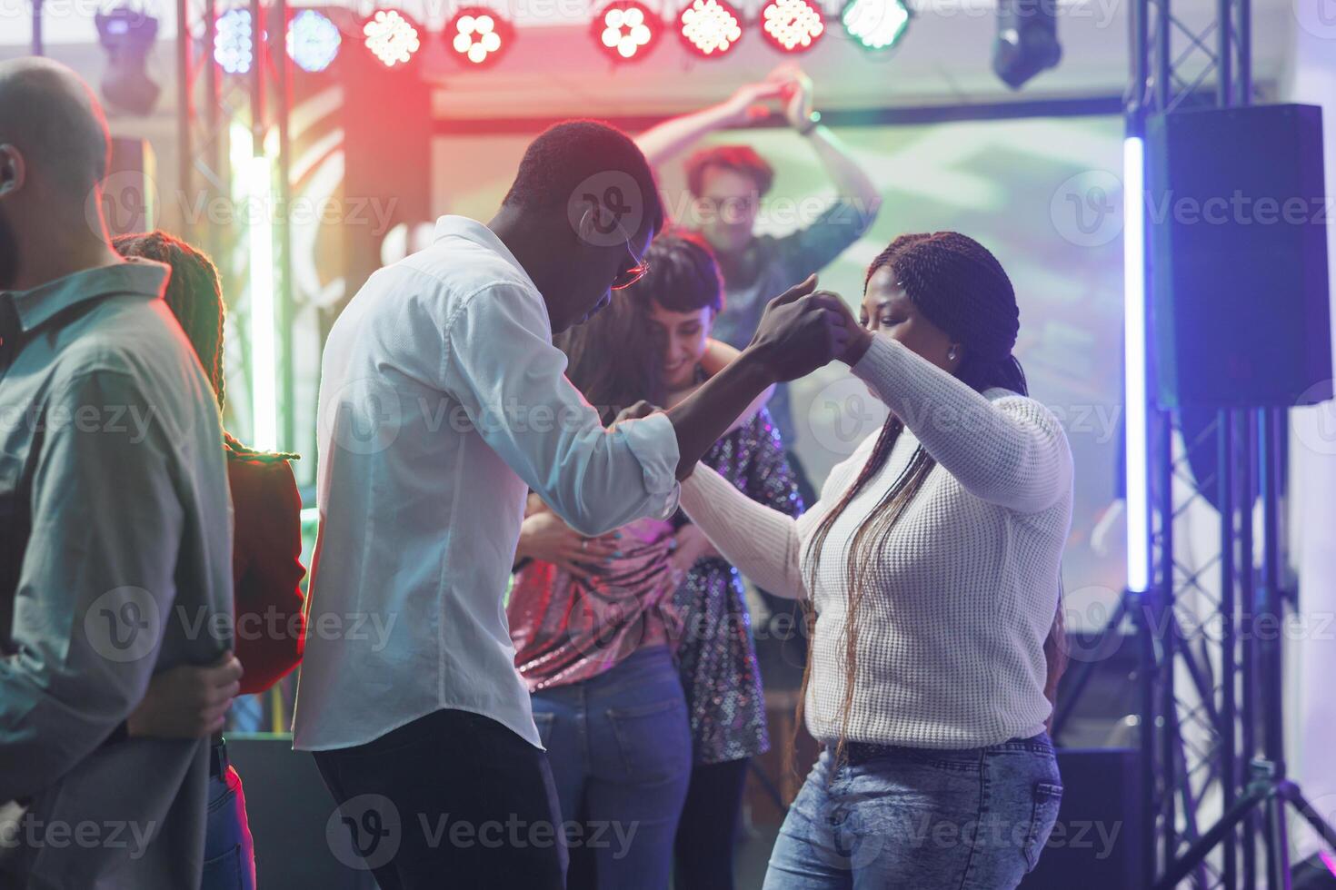 joven hombre y mujer amigos participación manos mientras bailando a Club nocturno fiesta. africano americano Pareja clubbing y Moviente en pista de baile mientras asistiendo discoteca reunión evento foto