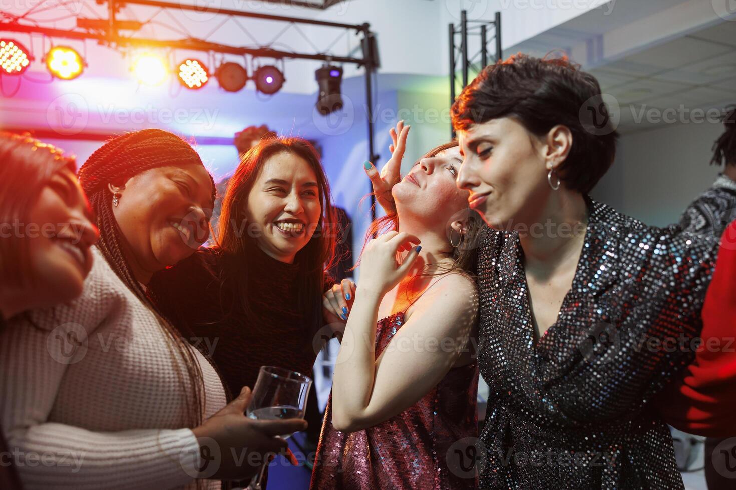 Cheerful smiling women drinking alcohol, hugging and partying together in nightclub. Carefree diverse girlfriends holding beverage glasses, laughing and having fun in club photo