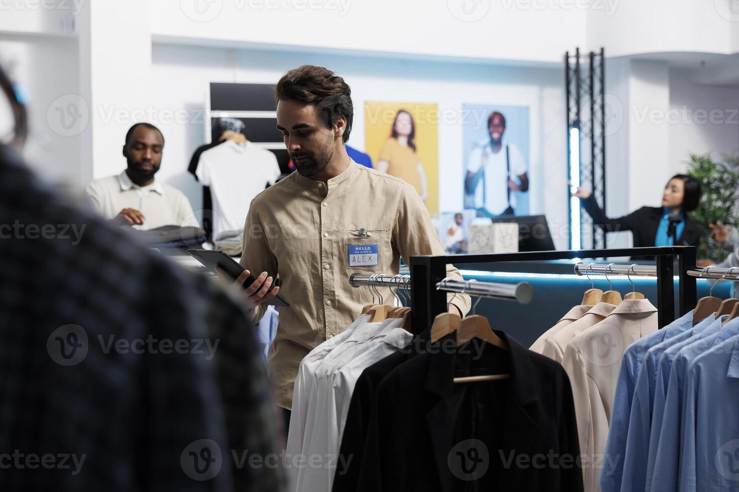 Clothing store manager using digital tablet and organizing merchandise to attract customers. Shopping center employee managing inventory and examining apparel hanging on rack photo