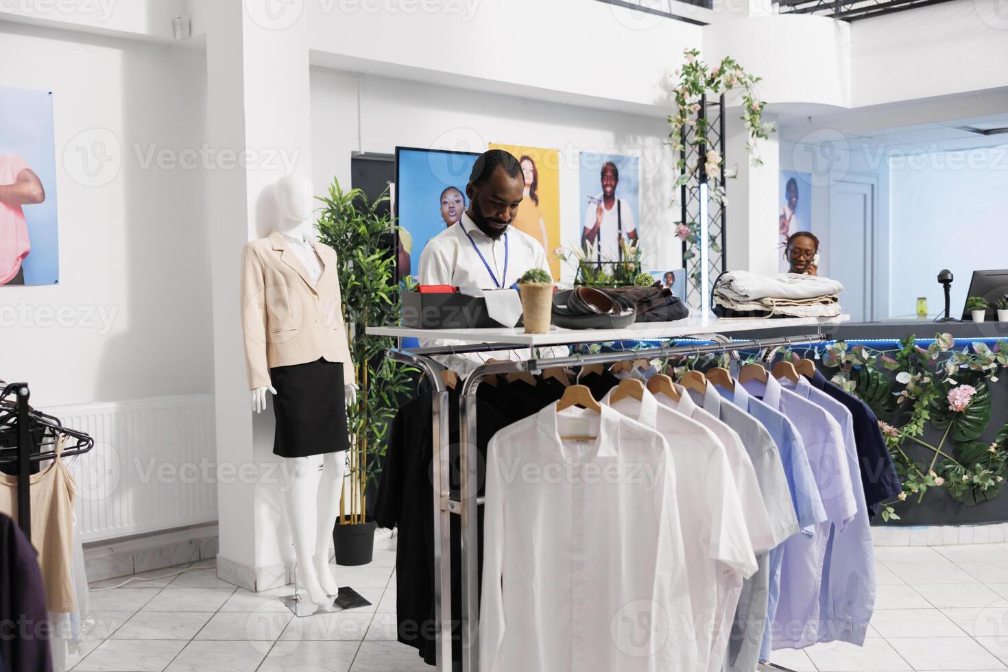 compras centro comercial africano americano asistente trabajando en Moda almacenar, tendido fuera ropa para venta. sala de exposición hombre empleado comprobación mercancías y mostrando prenda en perchas para clientes foto