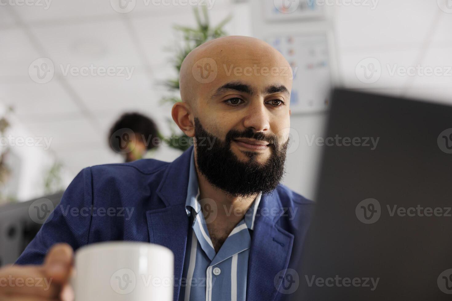 Smiling arab project manager checking customer email on laptop while working in business office. Company start up entrepreneur managing project on computer in coworking space photo