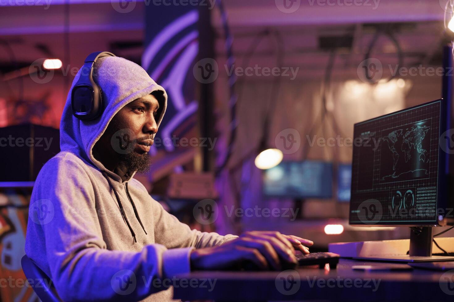 Hacker in headphones writing malware code and typing on keyboard. Internet criminal in hood listening to music in earphones and breaking into database server to breach data photo