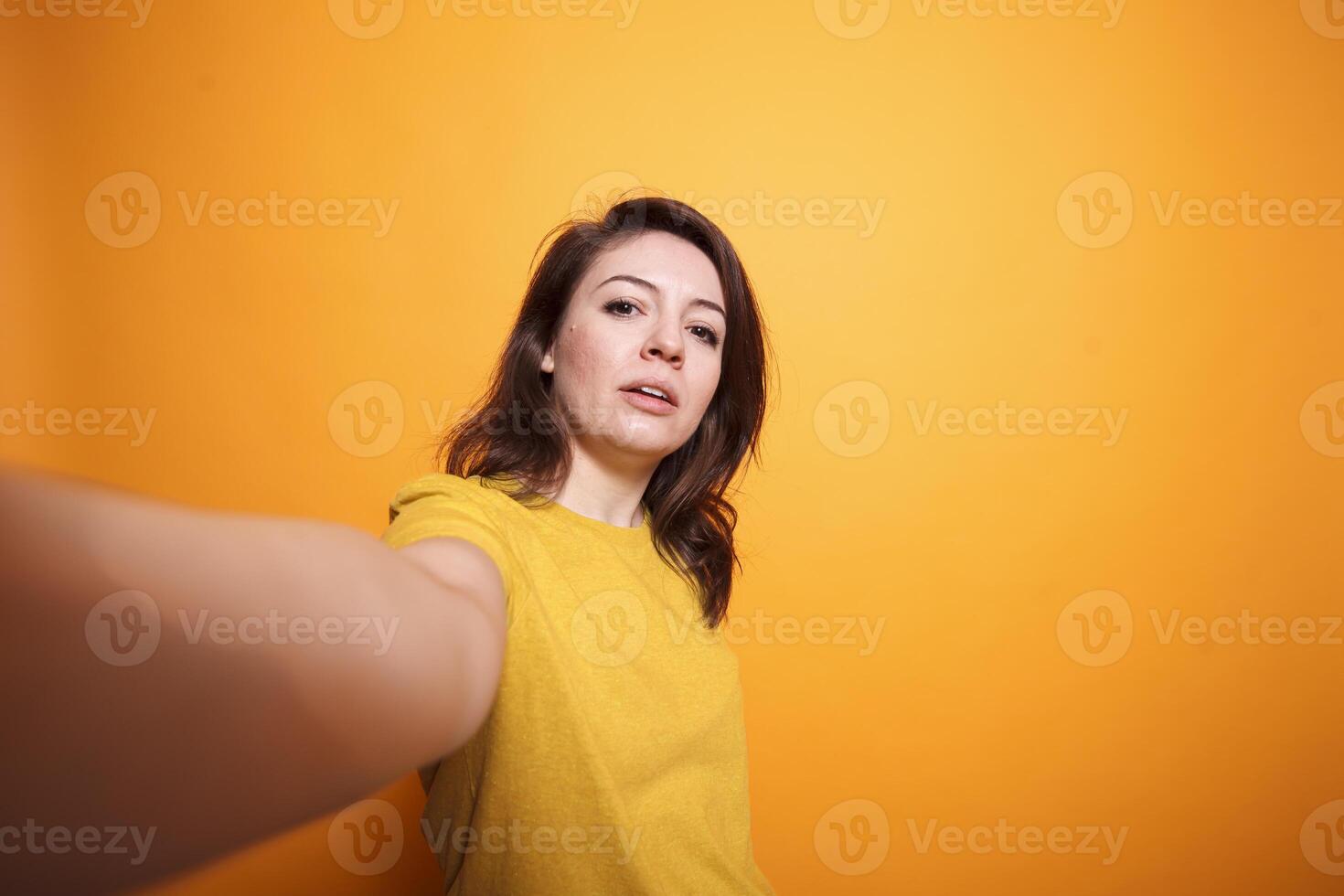 Cheerful gorgeous woman looking at camera taking picture using mobile device in studio with an isolated background. Smiling individual posing confidently for social media vlogging. photo