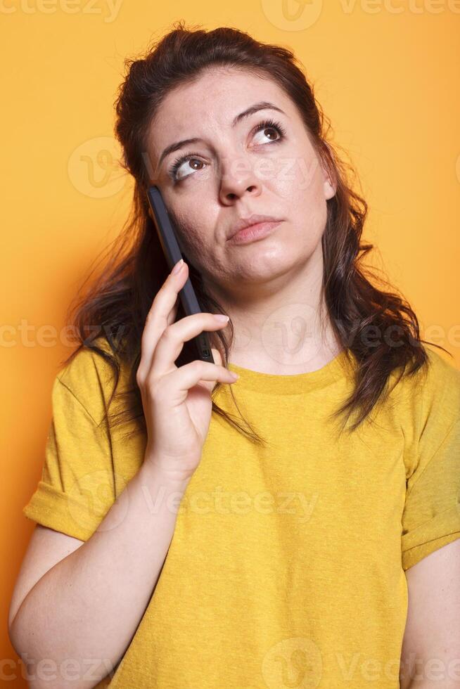 Portrait of female individual having important phone call conversation in front of isolated background. Close-up of woman in thoughts while talking on her mobile device with friends and family. photo