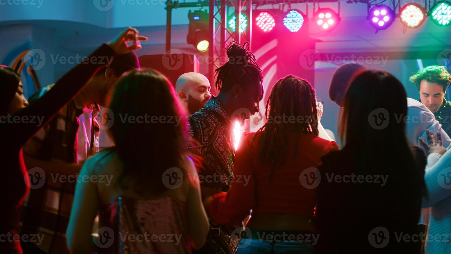 Young adults doing cool dance moves at club, partying together and having fun on electronic music. Diverse crowd of people enjoying night out with live performance on dance floor. photo