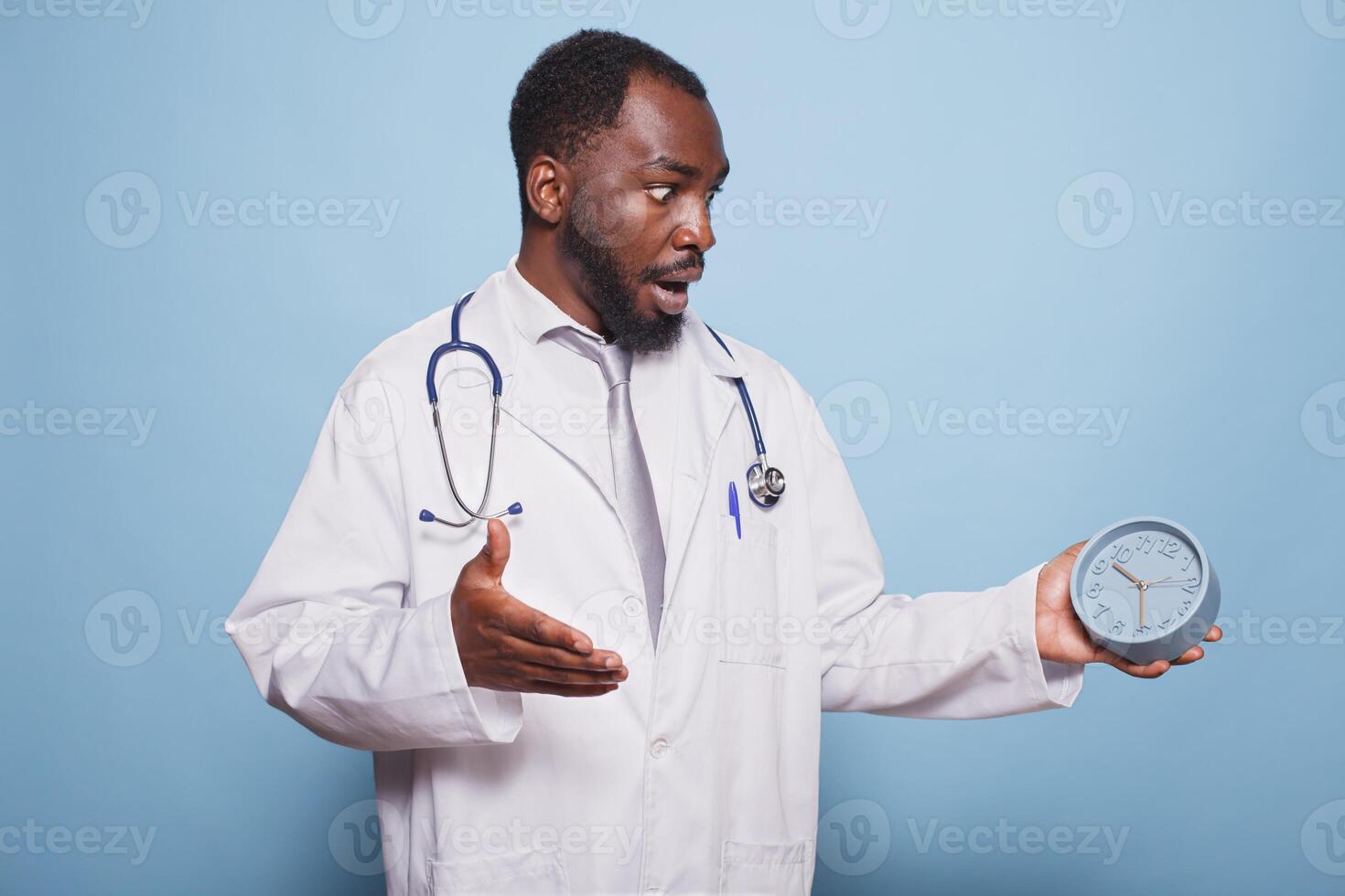 African American general practitioner shockingly looking at clock before a patient medical consultation. Black doctor appears to be in a panic, rushing and experiencing a healthcare emergency. photo