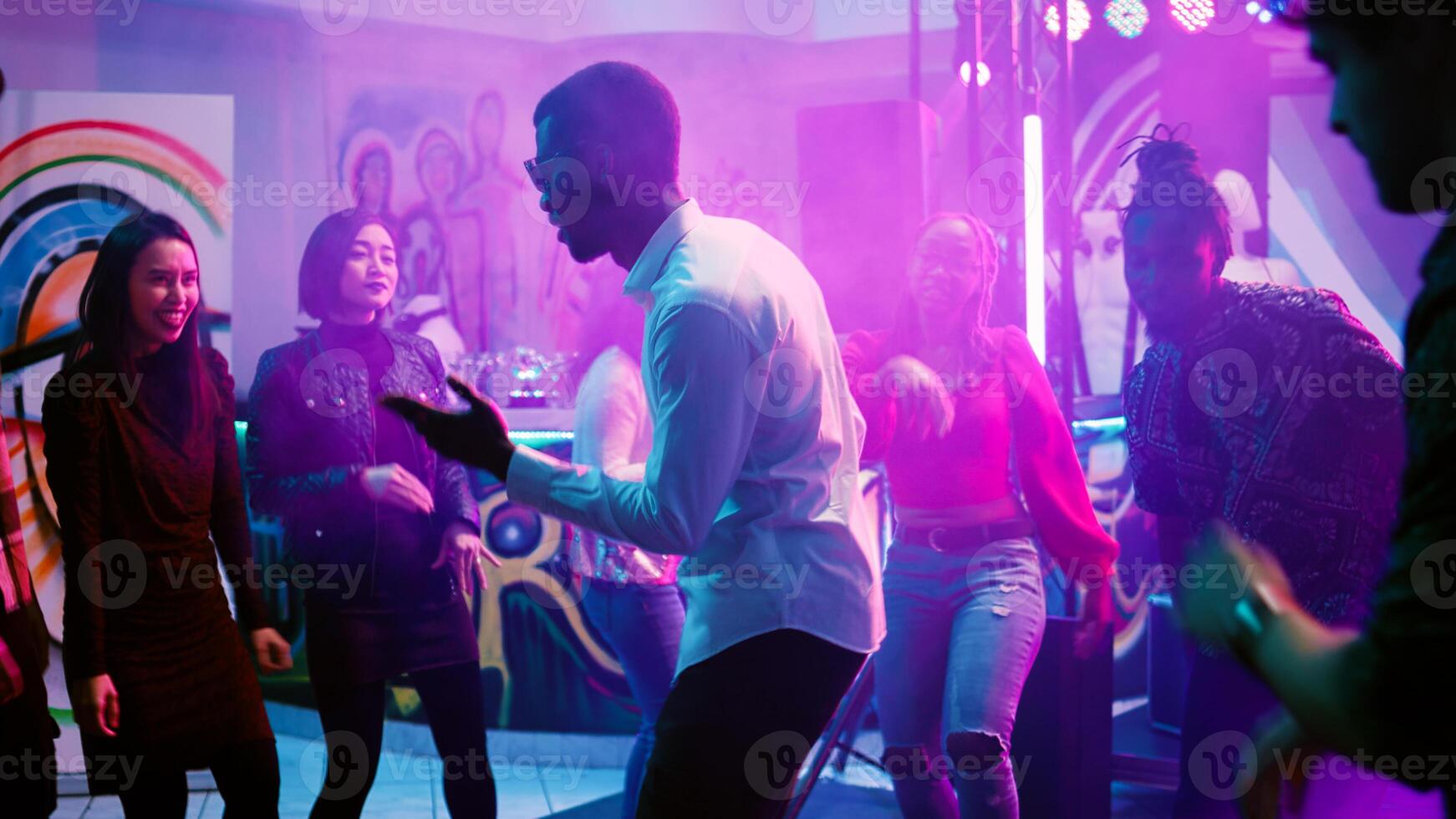 Multiethnic group of friends dancing, feeling happy at disco party on dance floor. Young adults enjoying nightlife with music and drinks, having fun with funky dance moves. Handheld shot. photo