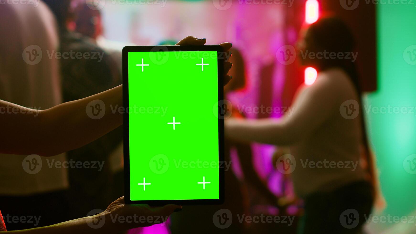 Girl showing greenscreen display at club holding blank chroma key display at party on dance floor. Modern person using isolated mockup screen with copy space template on device. Tripod shot. photo