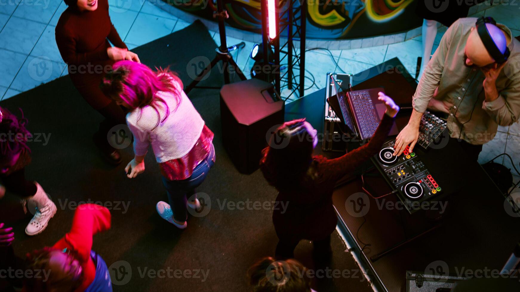 Happy persons having fun on dance floor with DJ music mix, partying with spotlights and audio performance. Group of people dancing and clubbing with electronic funky beats. Handheld shot. photo