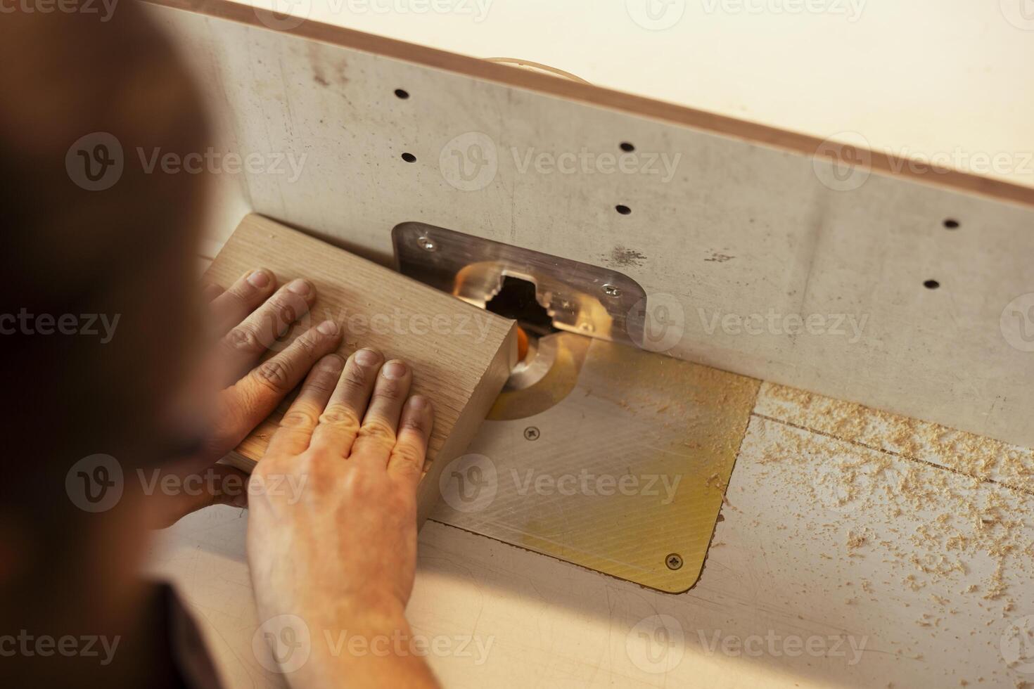 Carpenter in studio puts wood block through spindle moulder, creating smooth edges on wooden pieces. Cabinetmaker in carpentry shop using heavy machinery to craft strong seamless joints for furniture photo